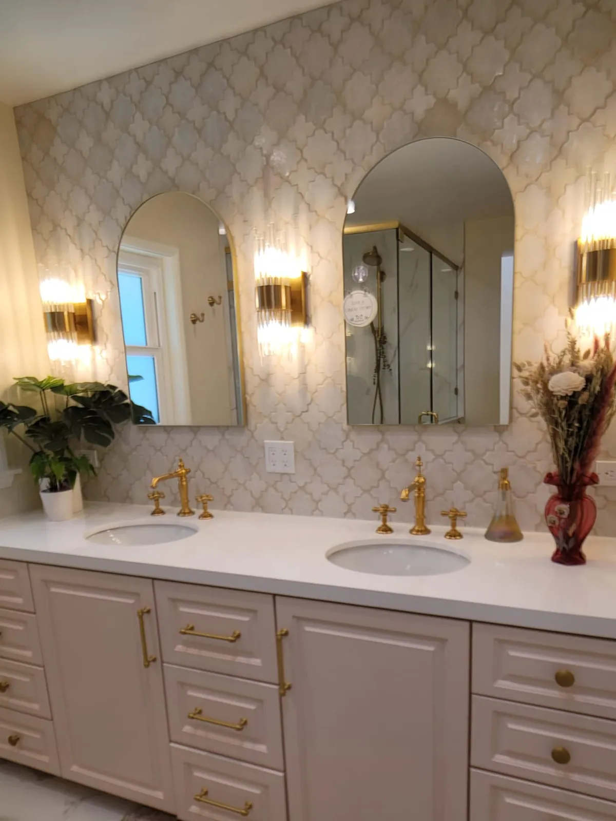The same primary bath after renovation by CCSI — double vanity, arabesque stone wall, arched mirrors, and brass fixtures