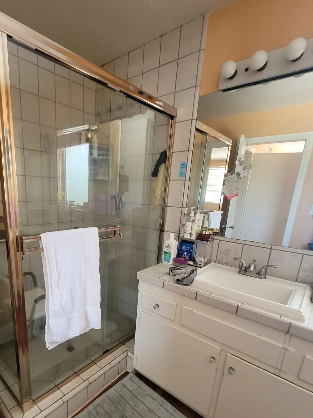 Primary bath before renovation — white square tile, brass-framed shower enclosure, and a tile-counter vanity